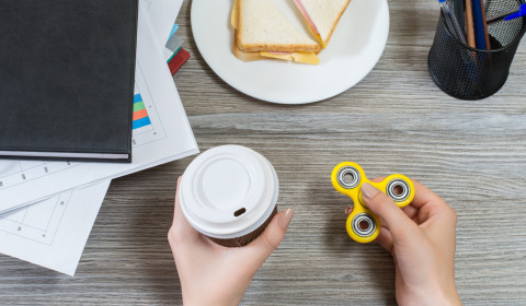 A person holding a coffee cup in one hand and a fidget spinner on the other hand