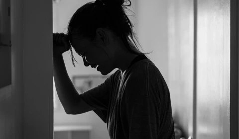 A black and white image of a woman putting her head on a wall in sadness