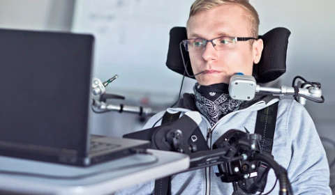 A physically disabled man using a laptop with assistive technology
