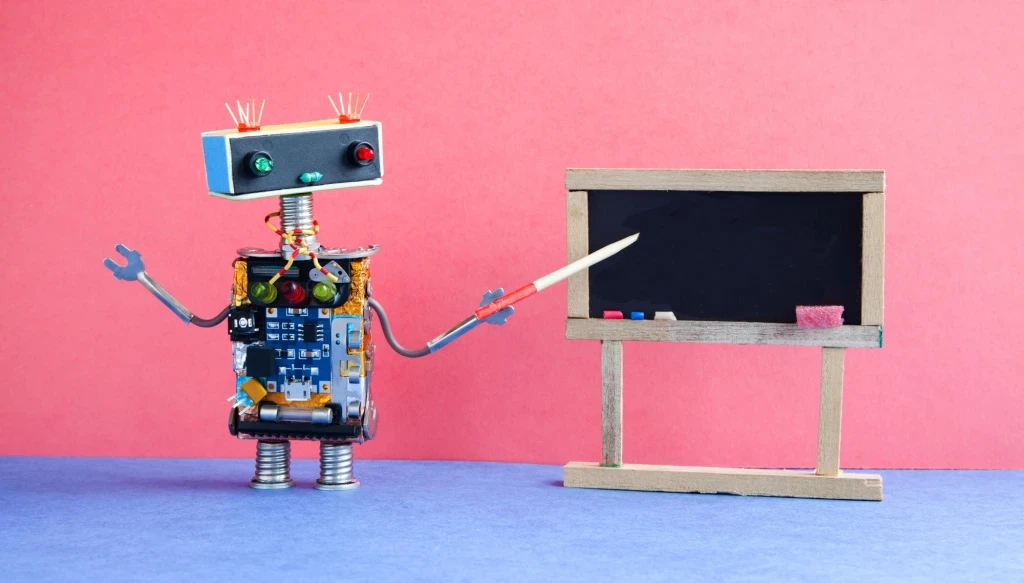 A robot made out of different materials using a pointer at a small chalkboard