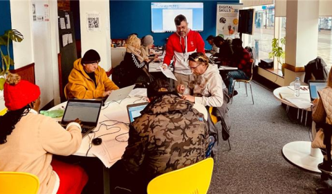 Photograph of a group of people working on laptops in a bright room with blue walls.