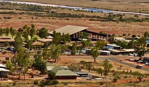 Aerial view of terracota coloured buildings, with trees and vehicles, and a river in the background.