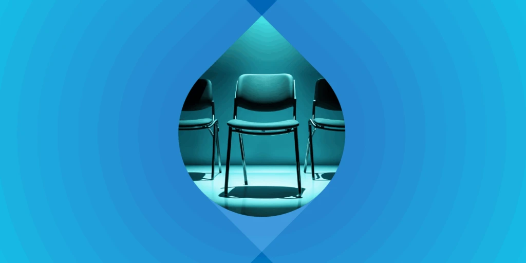 Photograph of a row of office chairs on a blue background. One chair is in a spotlight.