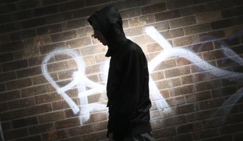 Photograph of the shadow of a young person in front of a wall with graffiti on it.