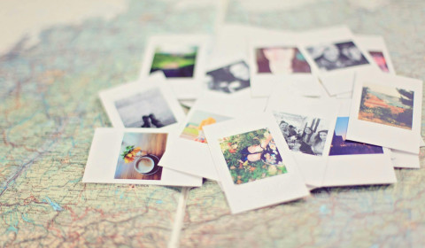 A pile of around 15 polaroid pictures scattered on top of a map. The pictures range from landscapes to coffee cups to selfies.