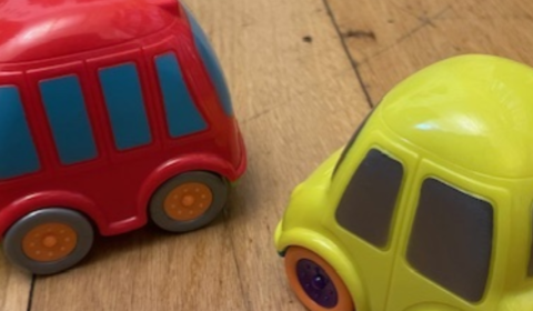 Two small toy cars, one red and one yellow, sitting on a wooden floor