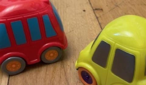 Two small toy cars, one red and one yellow, sitting on a wooden floor
